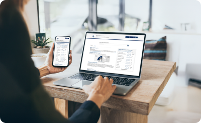 A woman with a phone in hand looking at the Weekly Investing report on her laptop